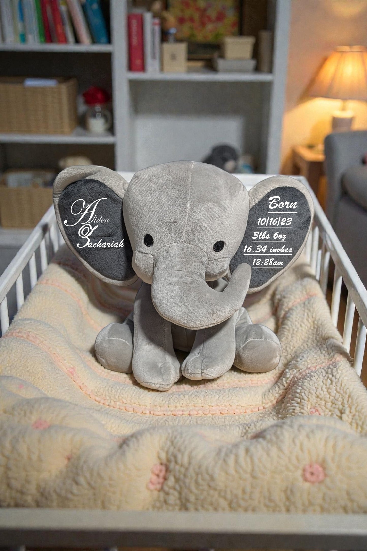 Gray elephant plush toy with personalized tags on a blanket in a crib