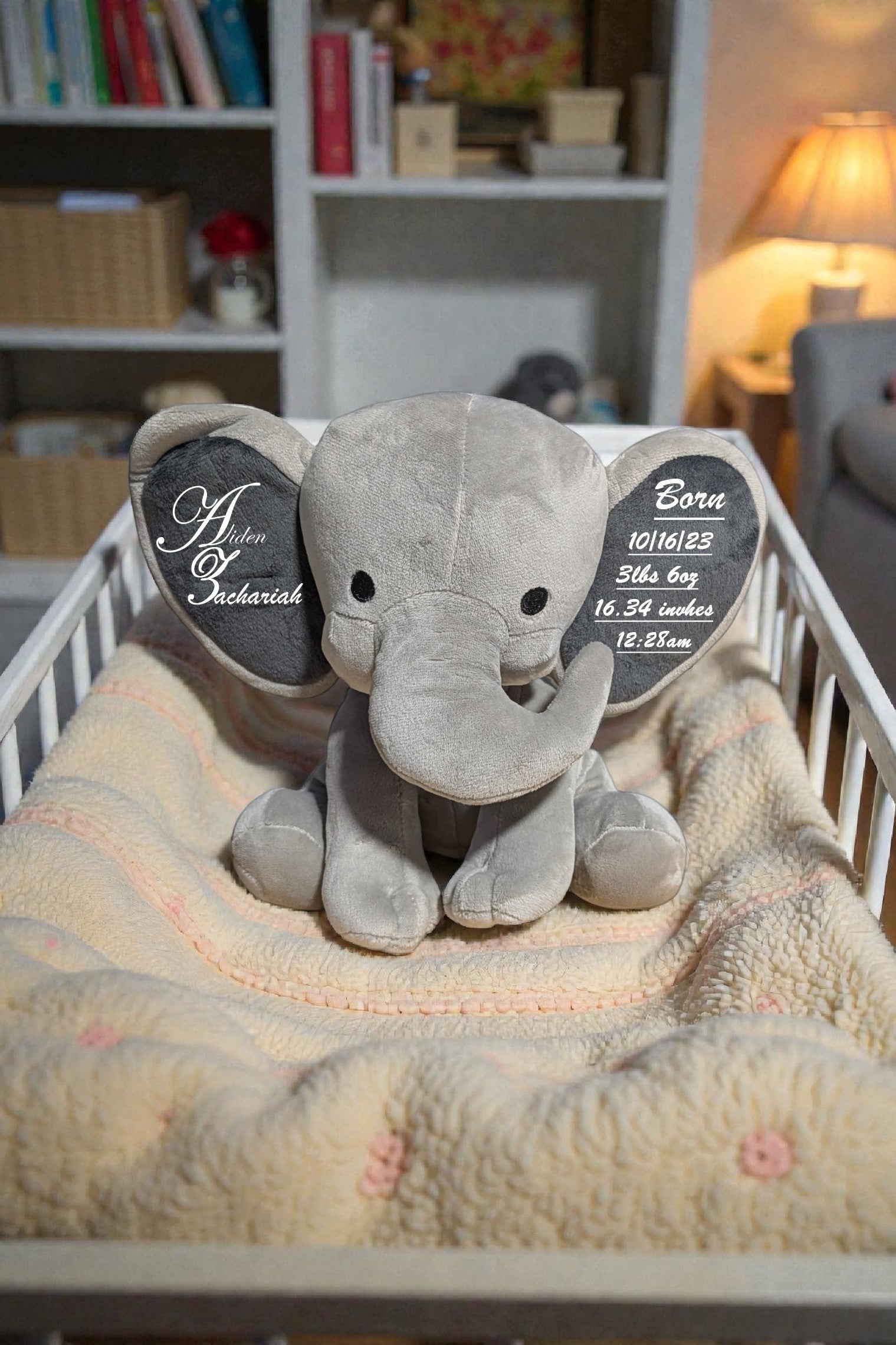 Gray elephant plush toy with personalized tags on a blanket in a crib
