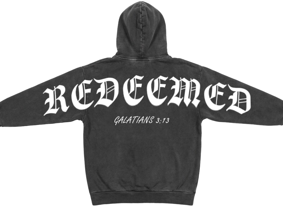 A black acid-wash hoodie shown from the back, featuring the word 'REDEEMED' in a large white gothic font across the upper back and 'GALATIANS 3:13' printed in smaller white script below it.