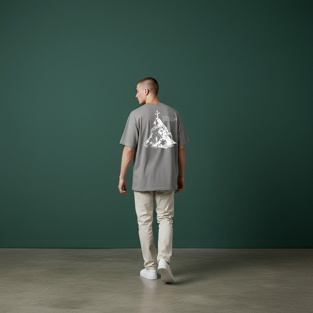Man wearing a gray t-shirt with a graphic design walking against a green wall.